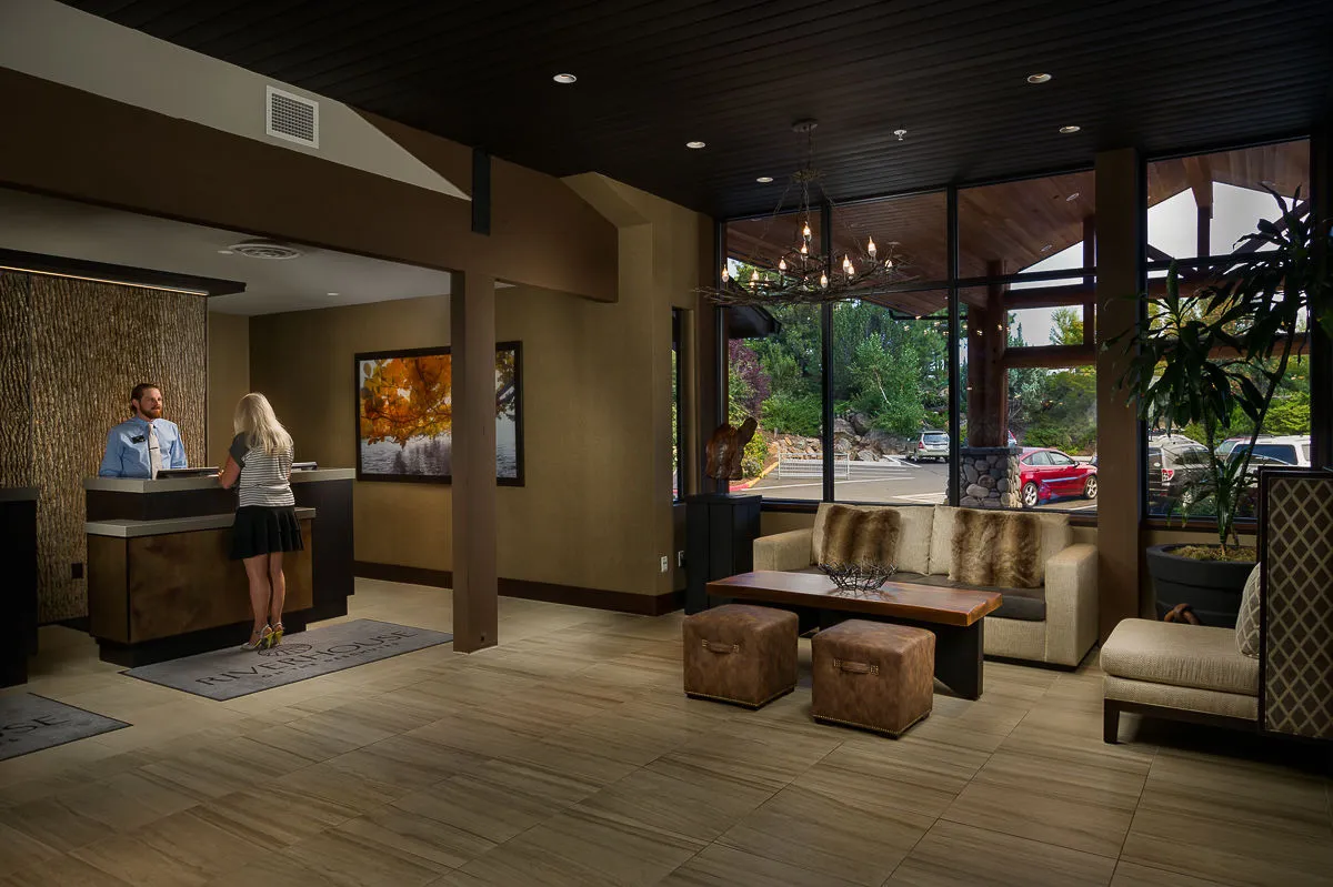 An inviting interior with a modern reception desk, comfortable seating, tasteful art on the walls, and expansive windows revealing lush outdoor scenery. The space is designed for welcoming guests, checking in, and relaxing before or after activities.