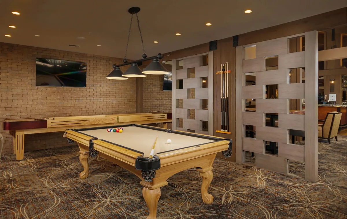 A game room featuring a pool table, seating area, and a wall-mounted TV. Wooden partitions offer a sense of openness, while people enjoy billiards, watch TV, and socialize, capturing the casual, fun side of the lodge experience.