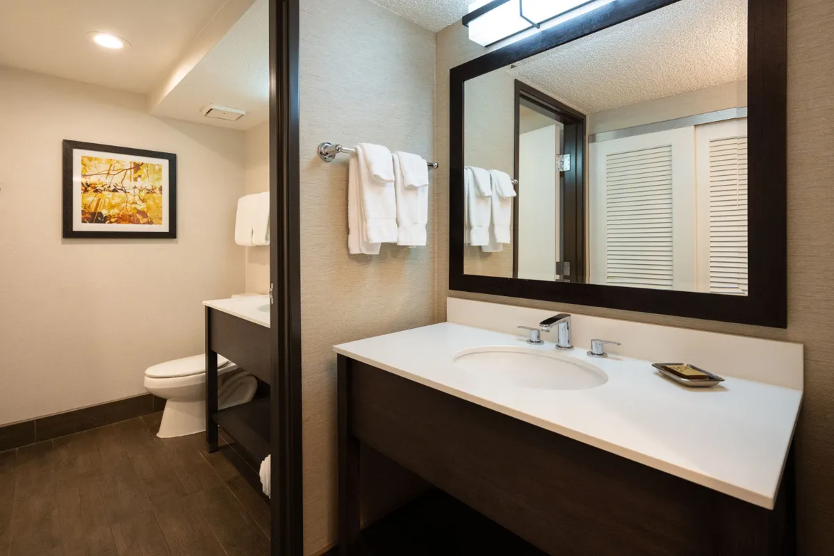 This interior image highlights a tastefully designed bathroom vanity area, featuring a modern sink, large mirror, contemporary wall art, and neatly arranged plush towels. The overall feeling is one of calm and spa-like relaxation, with soft lighting and thoughtful details that evoke the comforts of a high-end retreat.